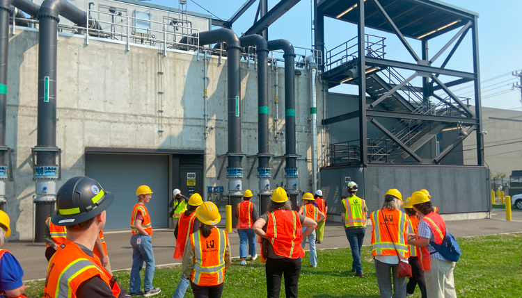 A group of 15 interns in hard hats and safety vests walk outside the Georgetown Wet Weather Treatment Facility
