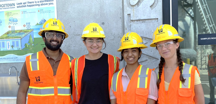 Four interns in hard hats and safety vests pose together smiling outside of the Georgetown Wet Weather Treatment Facility