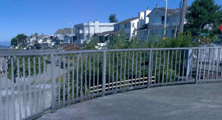 A railing on a concrete structure next to the beach. Houses along a street in the background. 
