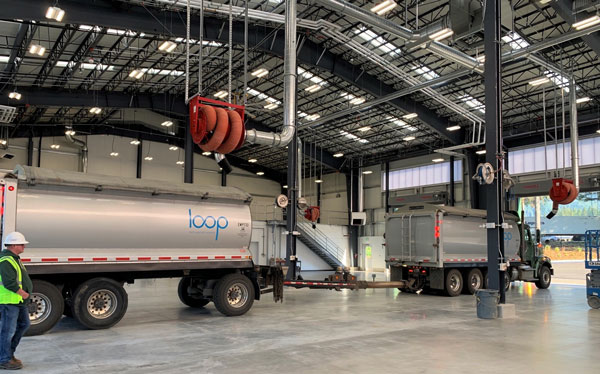 Man in yellow construction vest next to truck and trailer with "loop" logo on side of truck. Truck & trailer are inside new Loop vehnicle maintenance facility. 