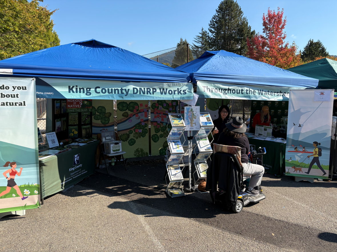 A photo of a community member and project team member talking at the King County Department of Natural Resources Booth at Salmon Days 2025