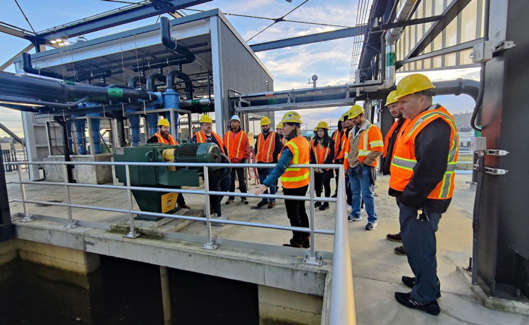 A group of people in orange safety vests and hard hats on a tour of the facility