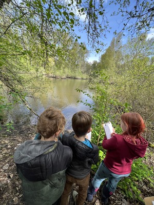 Elementary school children writing in their journal while looking out over a small lake during a field trip
