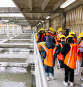 Elementary school group, wearing safety gear, writing in notebooks and standing next to wastewater treatment pools.