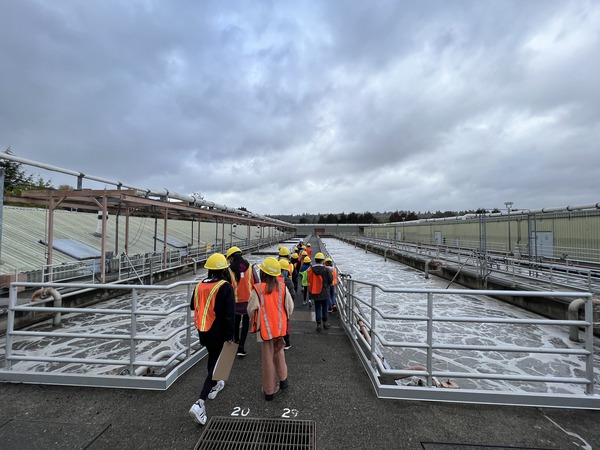 Students wearing PPE walking on a bridge over an aeration tank.