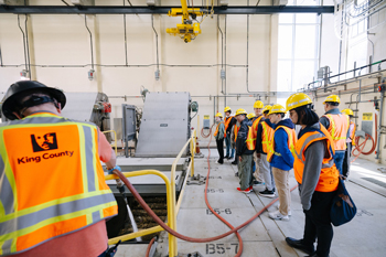 Group in safety gear looking into trash removal area of wastewater treatment plant.