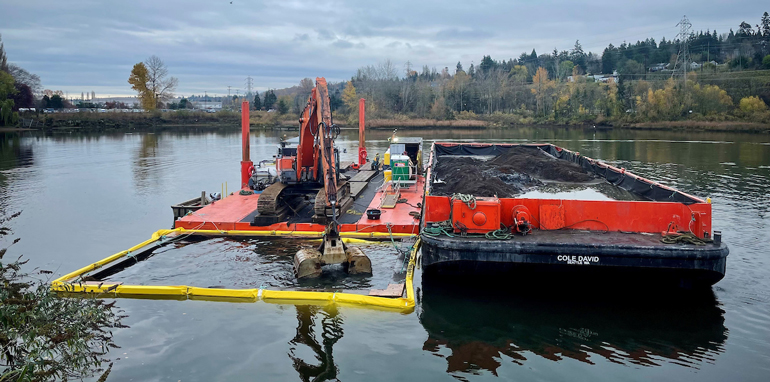 a dredge on a floating platform next to a barge, removing river sediment. 