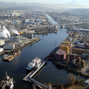This is an aerial photo showing the Lower Duwamish Waterway. In the distance, there are mountains and either side of the waterway is densely filled with industrial buildings.  