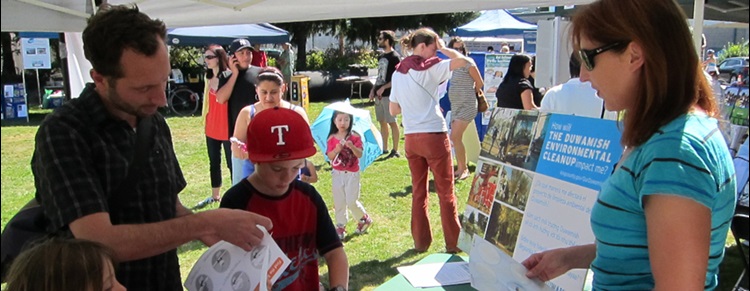 This photo shows a number of people at a festival – the sun is shining and people are looking at information about the cleanup of the Duwamish under a tent.