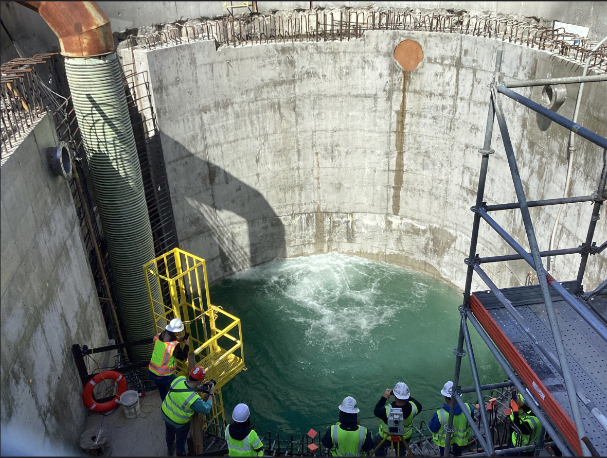 Construction workers observe water entering a large concrete shaft during a breakthrough at the Ship Canal Water Quality Project site.