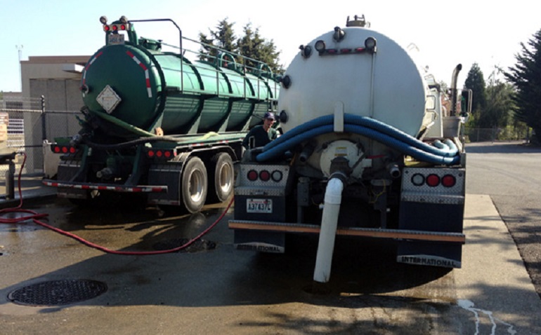 Two septage hauling trucks parked on a concrete strip. A pipe is connected from the tank of one of the trucks into a hole in the concrete.