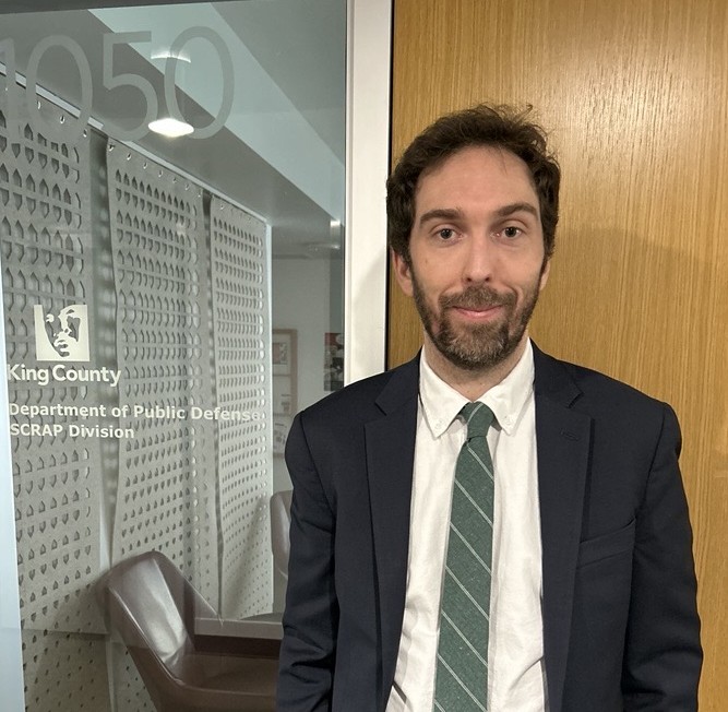 Colin O'Brien, a family defense attorney, pictured in front of his division's office wearing a dark suit, white shirt, and green tie.