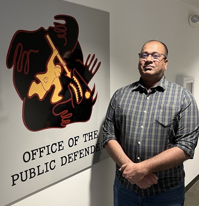 Paralegal Saneel Kumar standing next to artwork that reads Office of the Public Defender