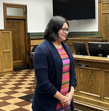 Attorney Selena Alonzo standing in a courtroom with hands clasped in front of her wearing a dark blue jacket and striped shirt