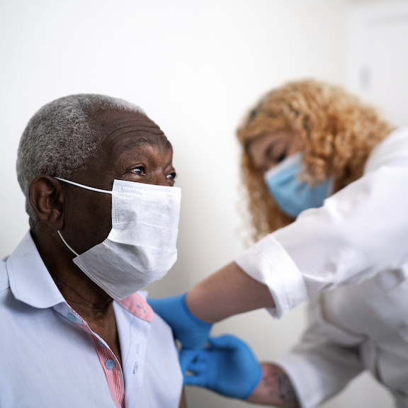 Masked male patient receiving immunizations from a nurse