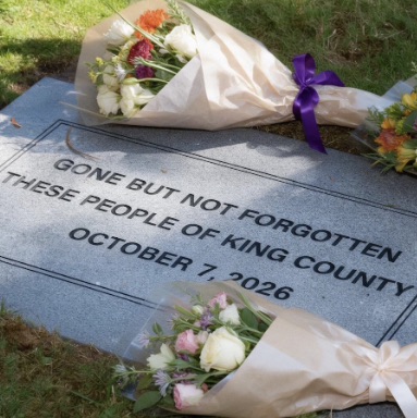 A close-up, high-angle shot shows a gray granite headstone with black lettering that reads "GONE BUT NOT FORGOTTEN THESE PEOPLE OF KING COUNTY OCTOBER 7, 2026." 