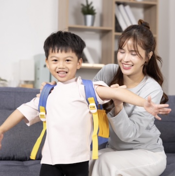 A mom helping her son put on his school backpack