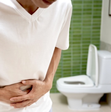 Image of a man holding his stomach due to cramps related to cyclosporiasis within a restroom