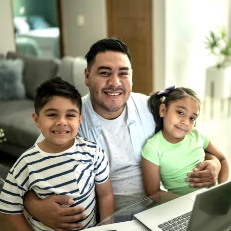 A Hispanic father holding his young son and daughter