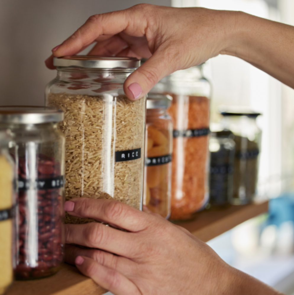 Someone grabbing bottled and labeled food items from a pantry shelf