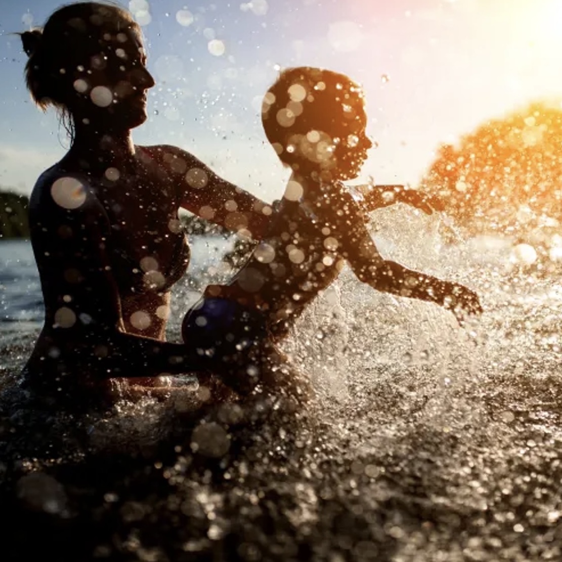 A young mother and child playing in the water at the beach on a sunny day.