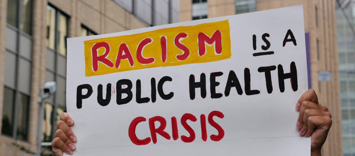 A person holding up a sign stating Racism is a Public Health Crisis