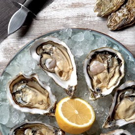 A plate of raw oysters and lemon with on oyster opener