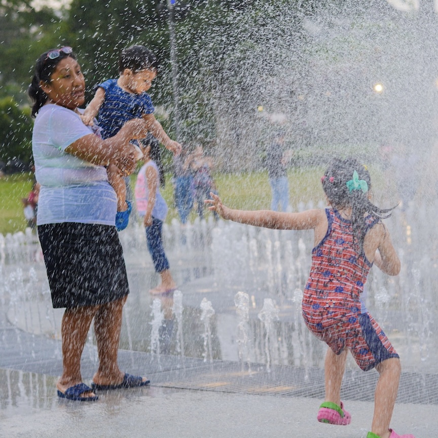 A woman and her children playing in a spray park.