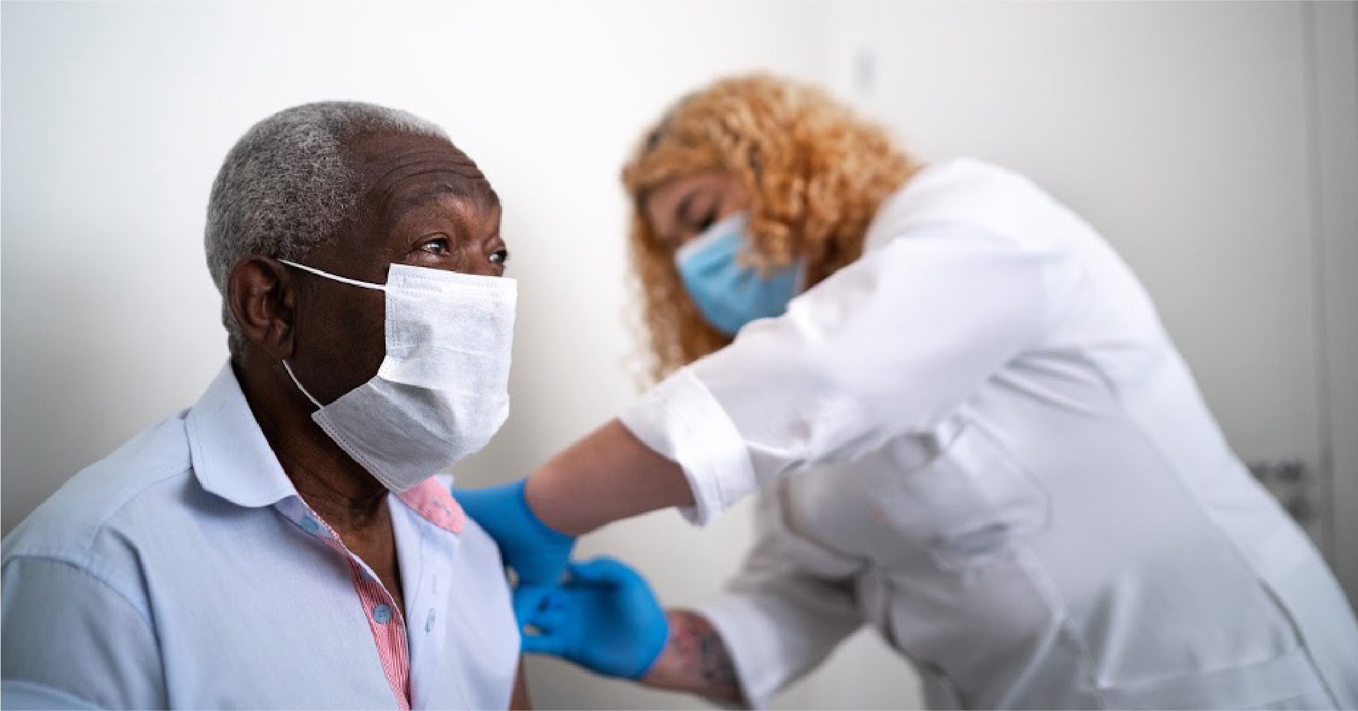 A nurse is giving immunizations to a patient. Both are wearing face masks.