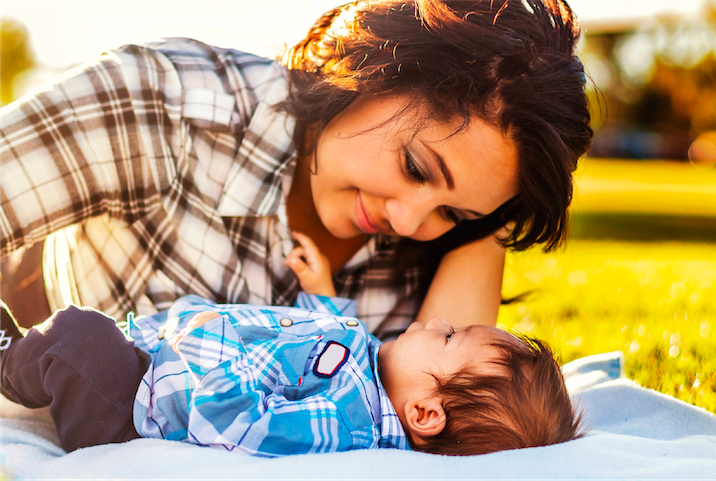 Mom looking down on baby while lying down in a sunny park