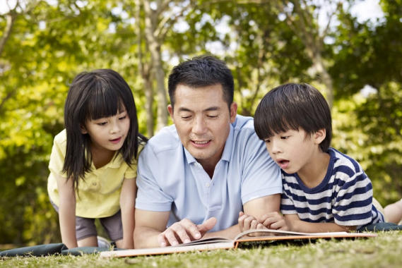 Single dad reading to his kids in a park