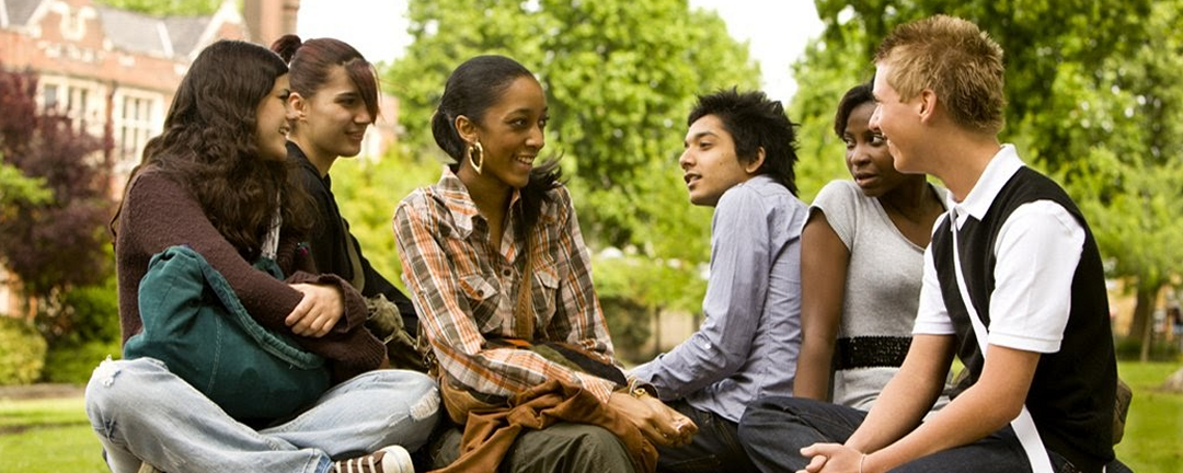 A group of high school students sitting on campus having a conversation.