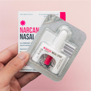 Image of someone holding up a box of Narcan brand nasal spray and an opened package of the spray nozzle device.