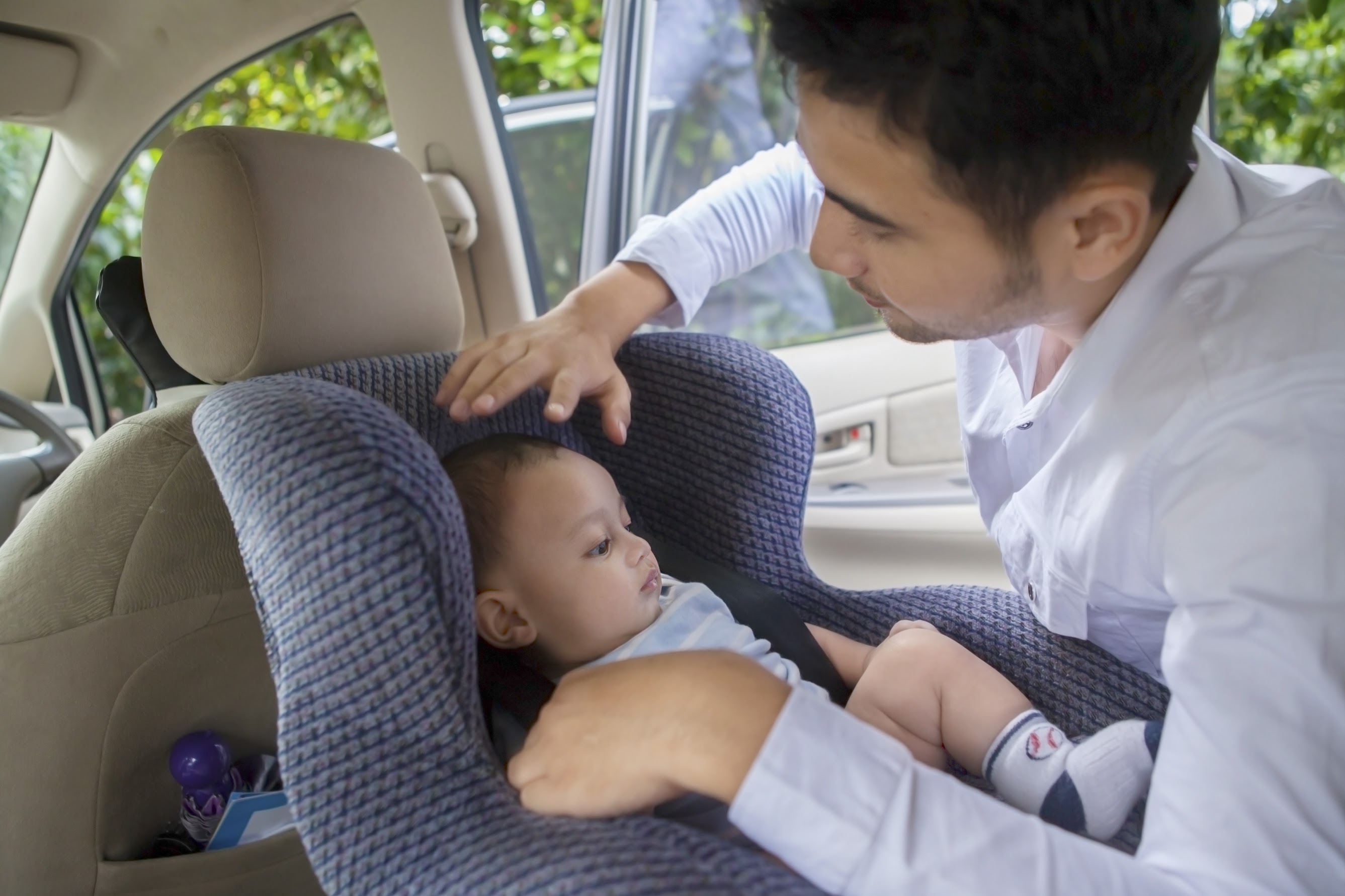 A father strapping in toddler in a child seat in a car