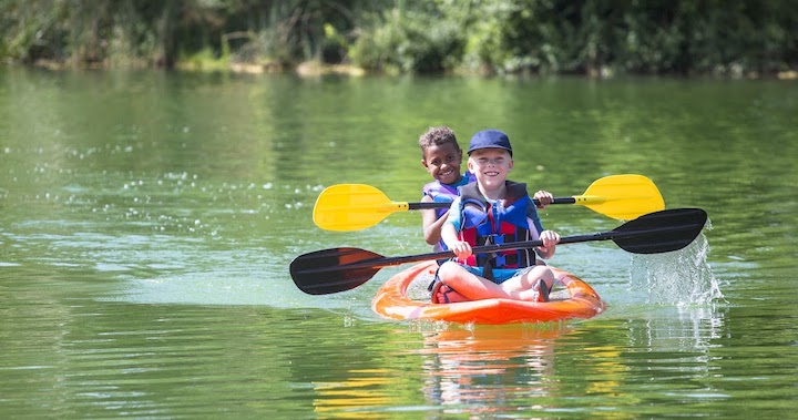 Two boys wearing life jackets in a kayak on a river