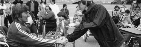 person in wheelchair shaking hands with person standing