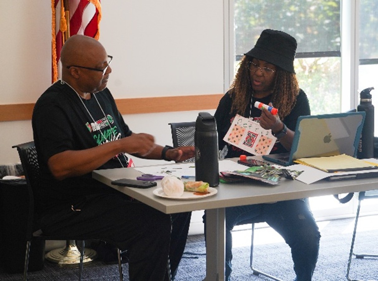two people work on an art project while sitting at a table in a meeting room