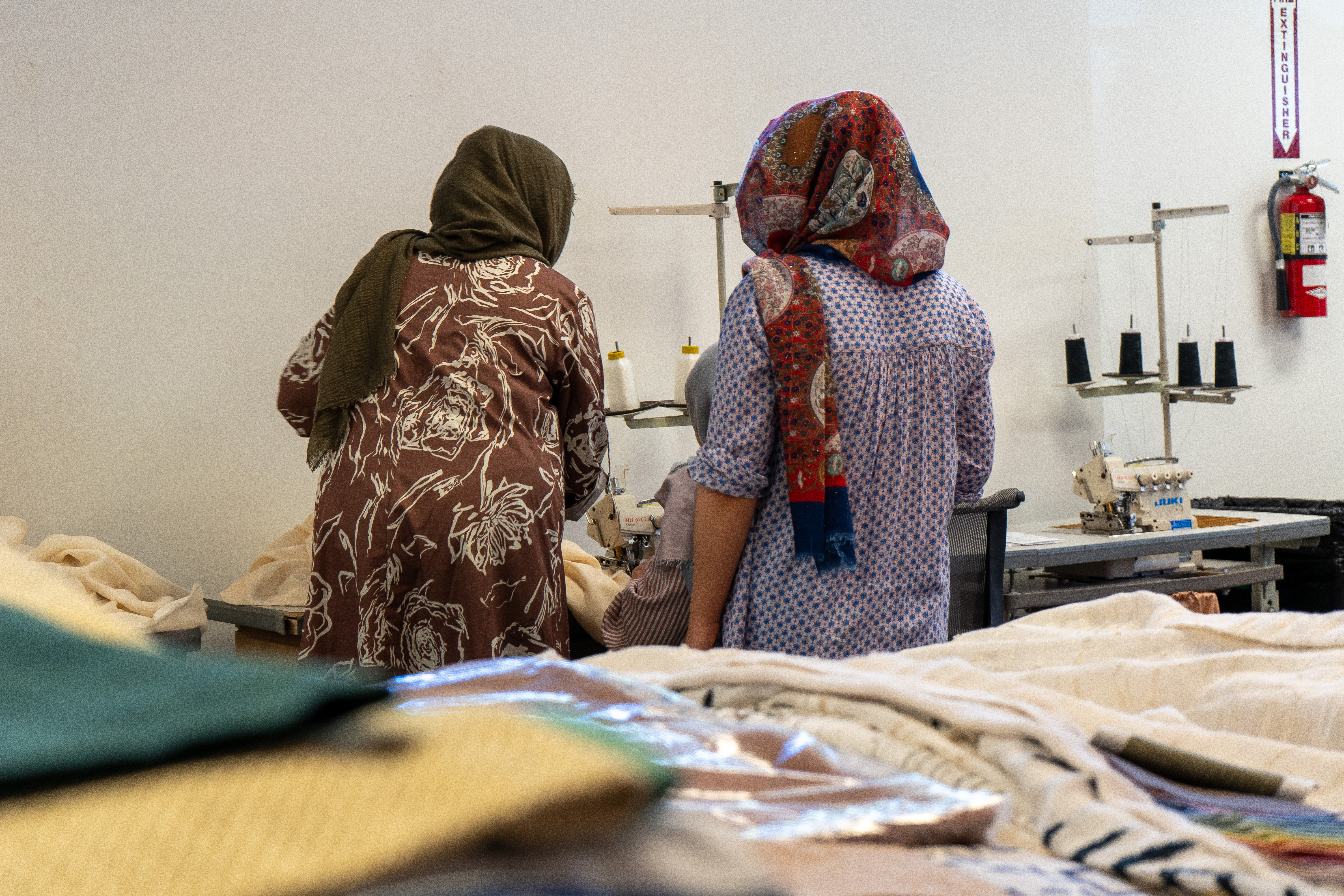 Two artisans sew, with fabric in the foreground of photo.