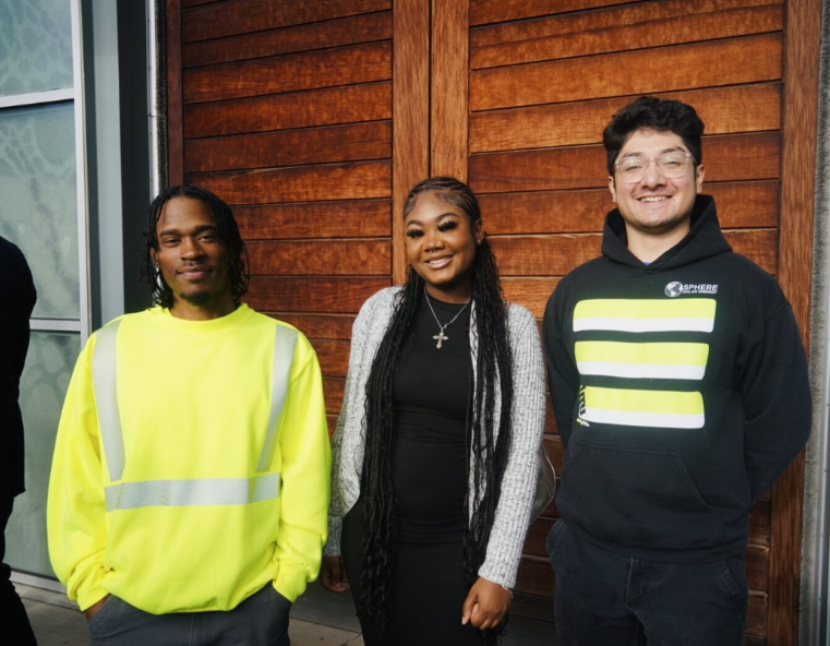 Image of three JumpStart graduates standing in front of a technology education center. One is wearing a high visibility work uniform.