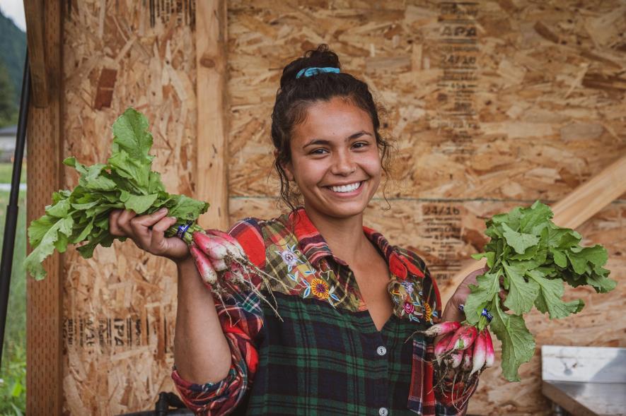 A smiling woman holding bushels of radishes.