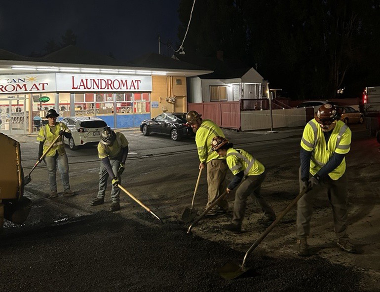 5 crew members working at night on the road in front of a laundromat.