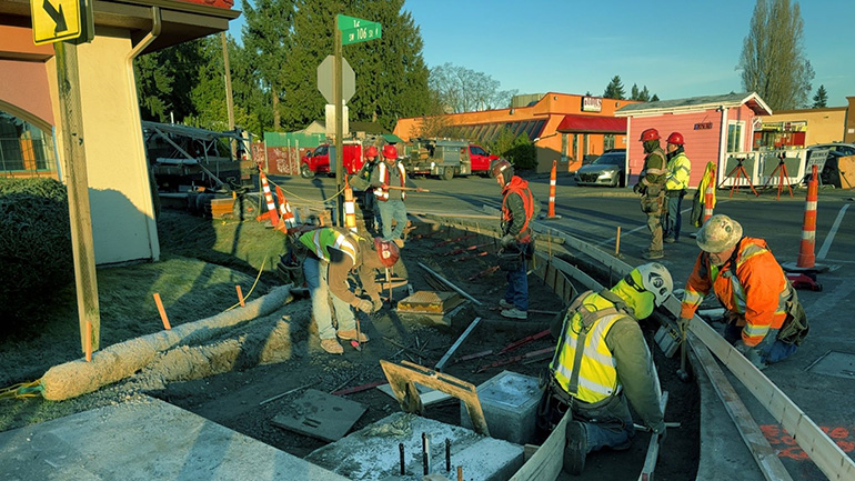 Road maintenance workers in ditch framing out new sidewalks.
