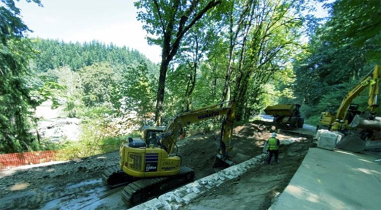 A tractor scrapes away old unstable soil and compacts the base using rocks to build a better base for construction. 