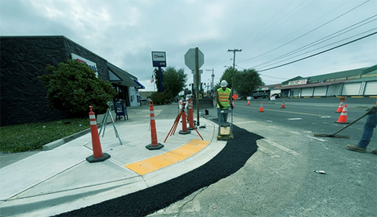 Raods worker smoothing freshly poured asphalt along a new curb ramp