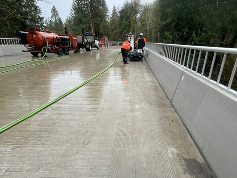 Road crew members use a pavement groover on a bridge deck.