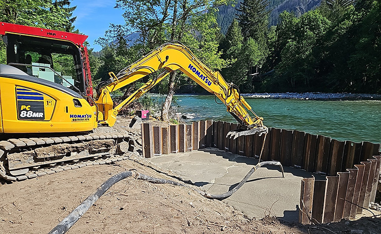 Heavy machinery pouring concrete along river bank.