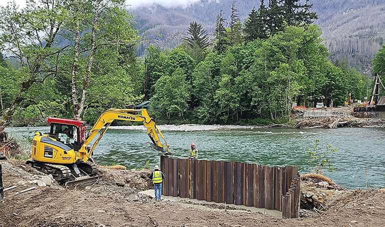 Crews on river bank installing steel piles