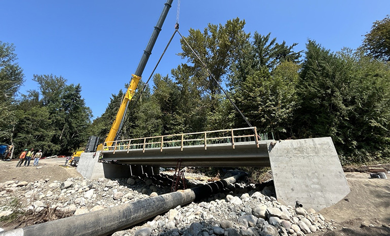 Crews using a crane to install bridge girders.