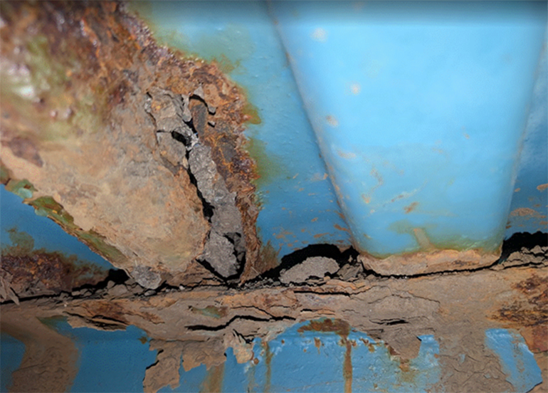 A view of a blue bridge from underneath showing blue metal and rust.