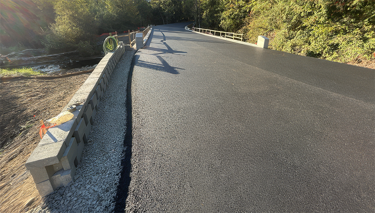 Fresh paved road with concrete barriers on the left side.
